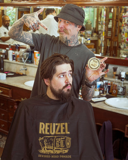 Reuzel X Liquid Death Severed Head barber cape with graphic design, featuring bold artwork and branding for salon or barber use.