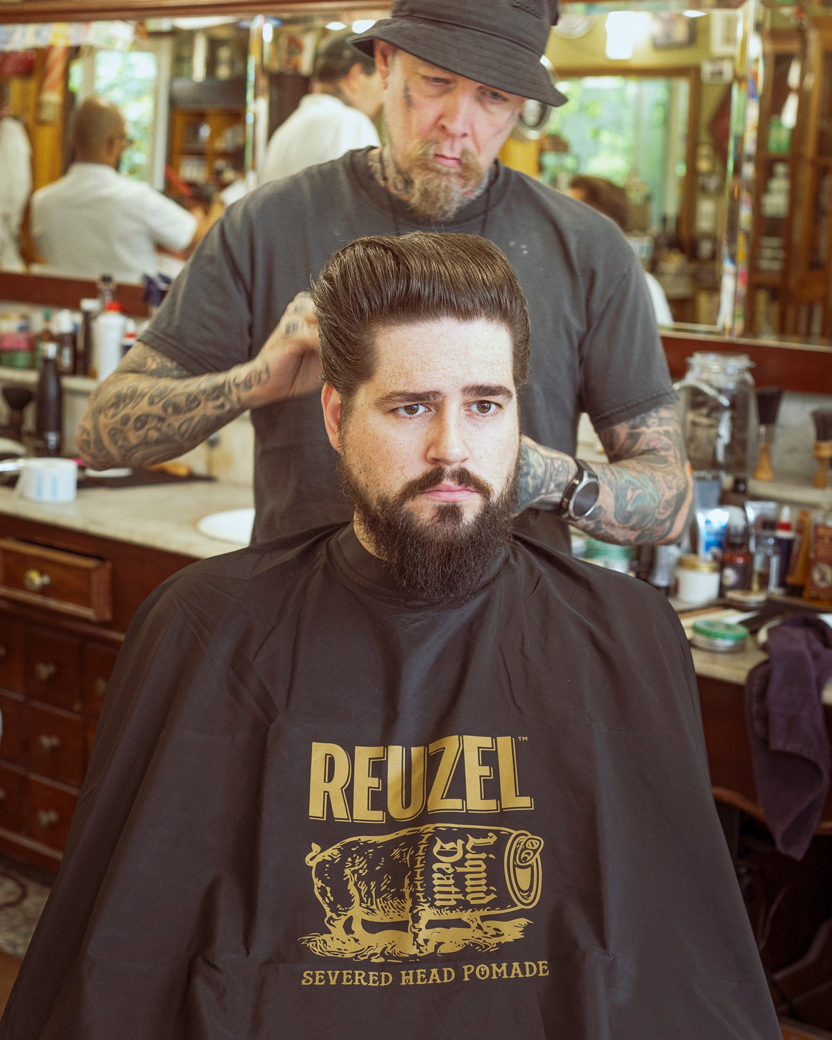 Reuzel X Liquid Death Severed Head barber cape featuring bold graphic design for hairdressing or barber use.